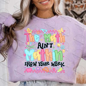 Puede incluir: Una sudadera lila claro con la frase "The Math Ain't Mathin' Show Your Work" en colores vibrantes. El dise&ntilde;o incluye s&iacute;mbolos y herramientas matem&aacute;ticas. Una sudadera informal y c&oacute;moda.