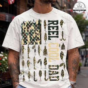 May include: White t-shirt with a fishing-themed design. The design includes a camouflage American flag, fishing lures, and the text "REEL COOL DAD" in green and camouflage. A great gift for a fishing enthusiast.
