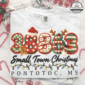 May include: White t-shirt with the text "Small Town Christmas" and the city name "Pontotoc, MS". The design features the numbers "2023" decorated with Christmas themes, including a Santa hat, reindeer antlers, and a snowman.