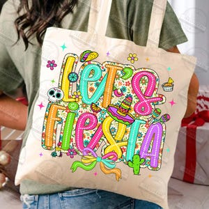 May include: A beige tote bag featuring the phrase "Let's Fiesta" in vibrant, playful lettering. The design incorporates a sombrero, maracas, and other celebratory illustrations, ideal for a party.