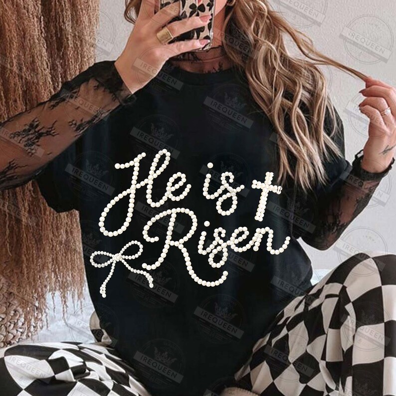May include: Black crew neck t-shirt with the text "He is Risen" in a white, cursive font. The shirt is paired with black and white checkered pants. The sleeves are sheer black lace.