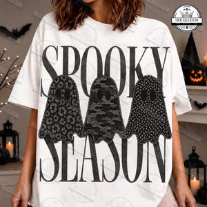 May include: A white t-shirt featuring the black text SPOOKY SEASON in a bold font. Three ghost illustrations are positioned between the words, each with a different black and gray pattern: leopard print, camouflage, and a dotted texture.