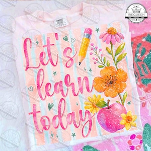 May include: A light pink t-shirt featuring the text Let's learn today in a pink script font. The design includes a yellow pencil, a pink apple, and various orange, yellow, and pink flowers against a background of vertical light stripes.