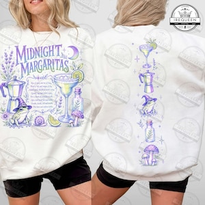 May include: A white crewneck sweatshirt featuring a graphic print of a frog wearing a witch hat, a margarita glass, a moka pot, and mushrooms. The text reads Midnight Margaritas with a potion recipe. The back shows a vertical arrangement of these icons.
