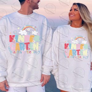 May include: White sweatshirts with a colorful "Kindergarten Dream Team" graphic. The design includes a rainbow, clouds, and school-themed elements. The sweatshirts are long-sleeved and suitable for the classroom.