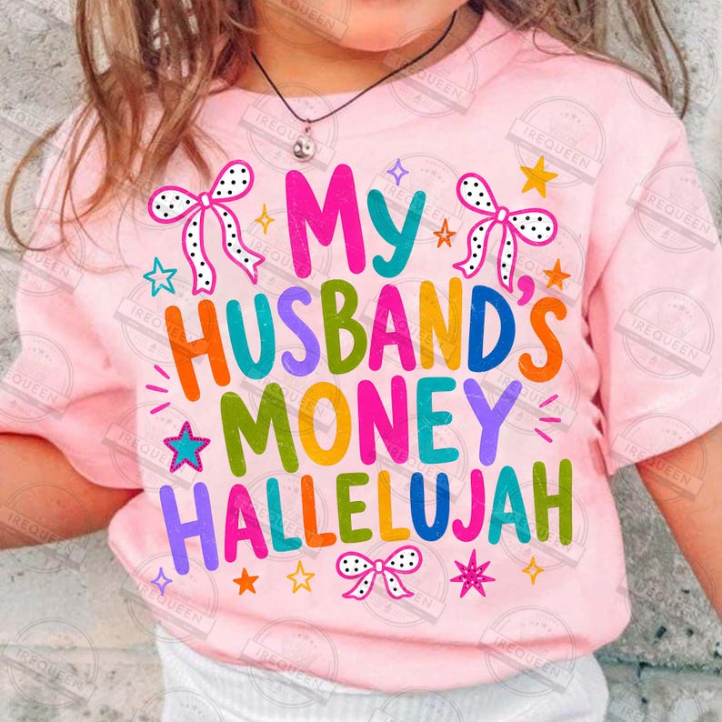 Pu&ograve; includere: Una t-shirt rosa chiaro con il testo colorato My Husband's Money Hallelujah. Il design include fiocchi bianchi a pois neri, insieme a varie piccole stelle nelle tonalit&agrave; del blu, arancione, giallo e rosa sparse sulla parte anteriore.