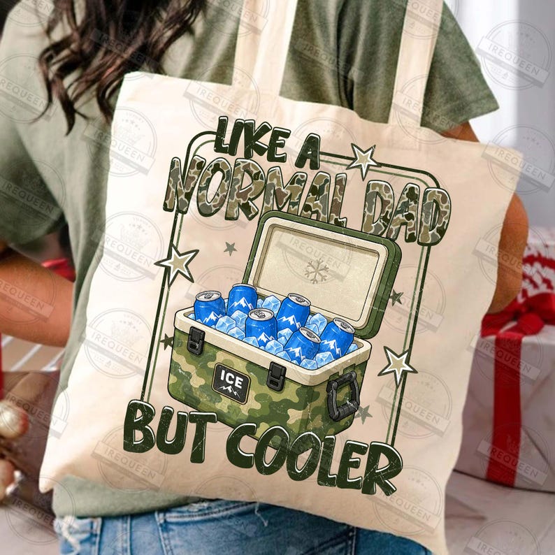 May include: A beige canvas tote bag with the text "LIKE A NORMAL DAD BUT COOLER" in black and green. The graphic features a camouflage cooler filled with blue cans and ice. The bag has a simple design with a rectangular shape.