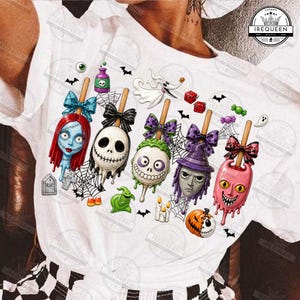 May include: A white t-shirt featuring a graphic print of five character-themed cake pops with bows, including Sally, Jack Skellington, and other figures. The design includes spider webs, bats, a ghost, a pumpkin, and a tombstone labeled RIP.