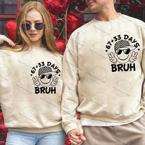 Pu&ograve; includere: Due felpe beige abbinate. Ognuna presenta una grafica di una faccina sorridente con occhiali da sole e un berretto a scacchi, con la scritta "67+33 DAYS BRUH". Le felpe sono in stile casual, adatte a coppie o amici.