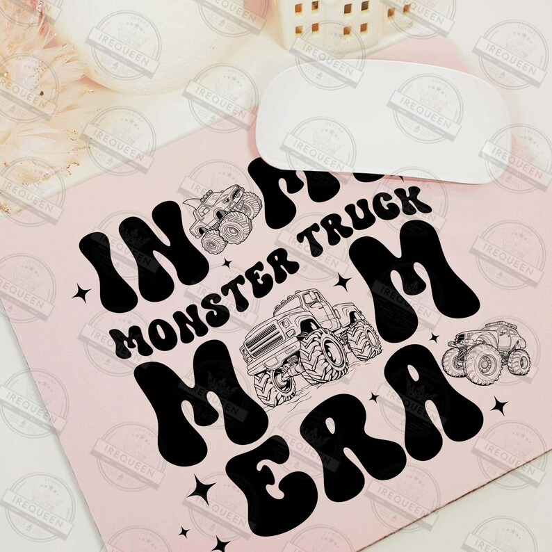 May include: A pink mouse pad with black text that reads "In the Monster Truck Mom Era". The text is in a retro font style. There are two black and white illustrations of monster trucks on the mouse pad.