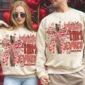 May include: Beige sweatshirts with a cross design. The cross is adorned with a pink ribbon patterned with red hearts. The text "I Will Praise Him in Every Season" is in red, with "Psalm 146:2" below the cross.
