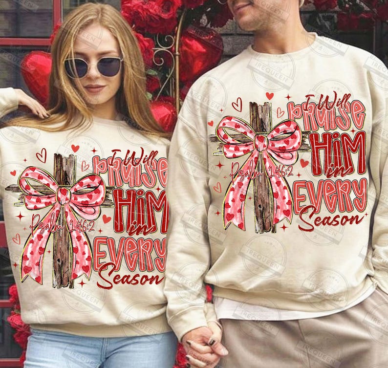 May include: Beige sweatshirts with a cross design. The cross is adorned with a pink ribbon patterned with red hearts. The text "I Will Praise Him in Every Season" is in red, with "Psalm 146:2" below the cross.