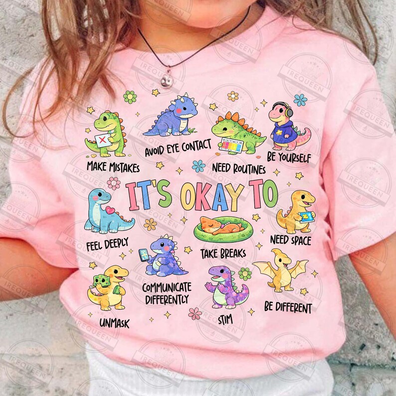 May include: A pink t-shirt with cartoon dinosaurs and phrases such as "It's Okay To" and "Need Space." The design includes various colours and is suitable for children. The t-shirt has a round neck and short sleeves.