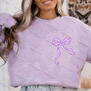 May include: A light purple sweatshirt with a large, lavender bow graphic on the front. The sweatshirt has a crew neck and long sleeves. The fabric appears soft and comfortable, suitable for casual wear.