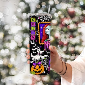 May include: A cylindrical tumbler featuring a black background with a white spiderweb pattern, a graphic of a character with long red hair, a white ghost dog, and an orange jack-o'-lantern. The text Sally is printed vertically in green.
