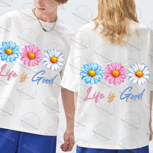 Pu&ograve; includere: T-shirt bianche con un motivo floreale a margherita blu, rosa e bianco, con la scritta "Life is Good" in una sceneggiatura colorata. Le magliette sono a maniche corte.