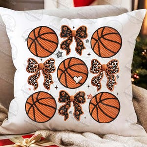 May include: White decorative pillow featuring a pattern of orange basketballs, leopard print bows, and basketball-themed bows. The basketballs have black lines and a heart design. Small star and plus symbols are also included.