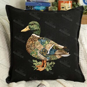 May include: Black square pillow featuring a detailed illustration of a mallard duck. The duck has a green head, brown and patchwork patterned body, and is set against a black background. The duck is standing on a bed of green leaves.
