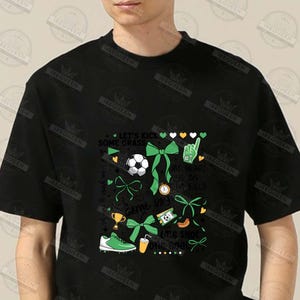 May include: Black t-shirt with a green, white, and gold graphic design featuring a soccer ball, bows, and the text "Let's Kick Some Grass", "My Heart Is On That Field", "Game Day", and "One Shot One Goal".