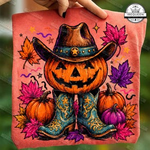 May include: A coral-colored t-shirt featuring a graphic of a jack-o'-lantern wearing a brown cowboy hat with a star, standing in blue cowboy boots. The design includes orange and purple maple leaves, small pumpkins, and scattered star shapes.