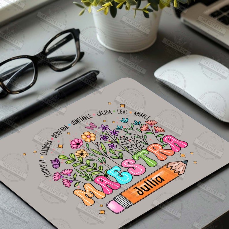 May include: A gray mousepad with a colorful illustration of the word "MAESTRA" with a pencil and flowers. The pencil is labeled "Jullia". The words "COMPASIVA CARINOSA DEDICADA CONFIABLE CALIDA LEAL AMABLE" are written around the flowers.