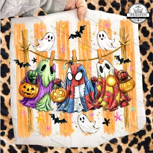 May include: A white fabric square featuring a graphic of three ghosts dressed in costumes hanging on a clothesline. The ghosts wear green, red-blue-white, and red-yellow patterns, holding orange jack-o'-lantern buckets. Bats and stars surround them.