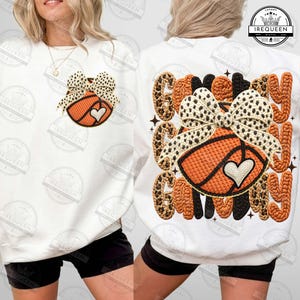 Puede incluir: Sudadera blanca con diseño de baloncesto, lazo y corazón. El baloncesto es naranja con detalles negros, y el lazo tiene un estampado de leopardo. El texto "Game Day Only" está en la parte posterior.