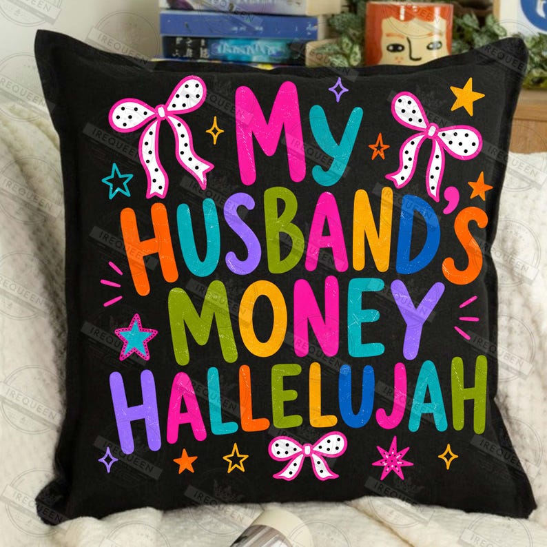 Pu&ograve; includere: Un cuscino quadrato nero con il testo colorato My Husband's Money Hallelujah in un carattere giocoso. Il design presenta lettere rosa brillante, arancioni, blu, verdi e viola, accentuate da fiocchi bianchi a pois e piccole stelle decorative.