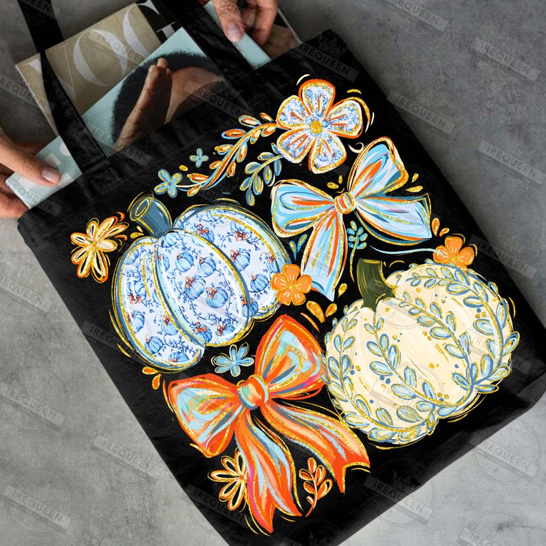 May include: Black tote bag featuring a colorful autumn design. The design includes pumpkins, bows, and floral elements in shades of blue, orange, and yellow. The tote bag is filled with books and magazines.