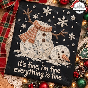 May include: A black t-shirt featuring an embroidered snowman made of white lace fabric, wearing an orange and white checkered scarf. The snowman has brown branch arms and dark buttons. The text reads: it's fine, i'm fine everything is fine.