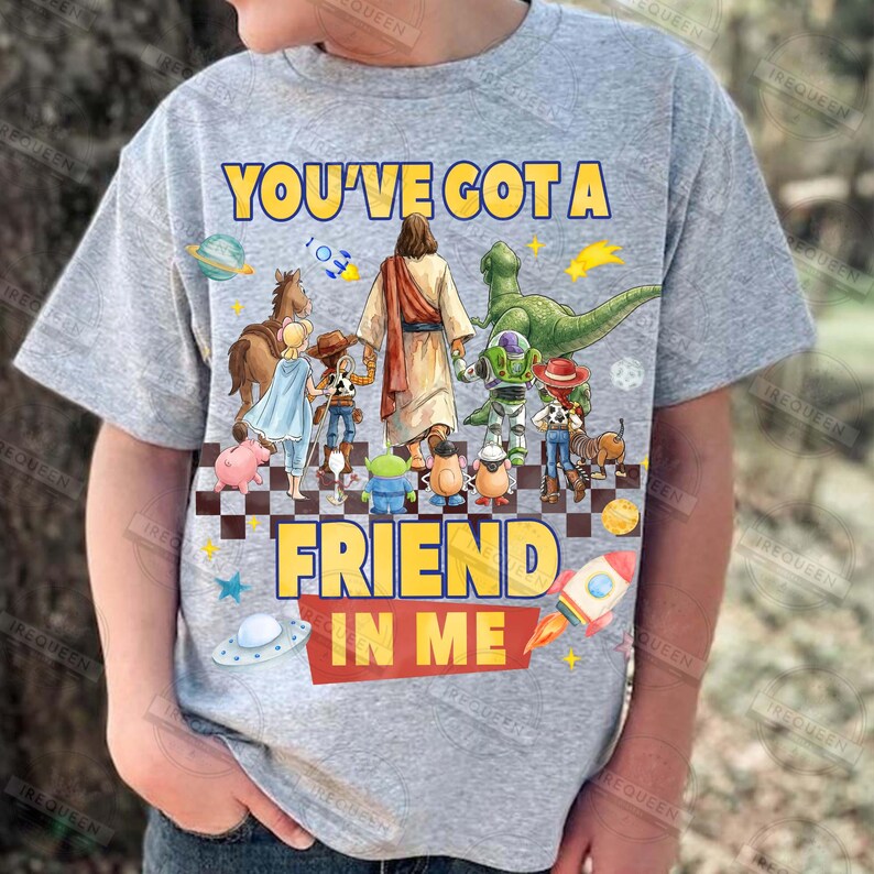 May include: A gray t-shirt featuring the text "YOU'VE GOT A FRIEND IN ME" in yellow. The graphic includes cartoon characters and a depiction of Jesus. A rocket, planets, and stars are also present.