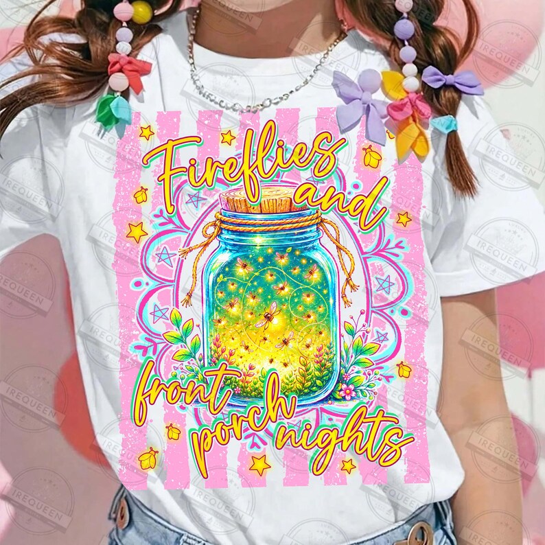 May include: White t-shirt featuring a colorful graphic of a mason jar filled with fireflies, with the text "Fireflies and front porch nights." The design includes pink stripes, stars, and floral elements.