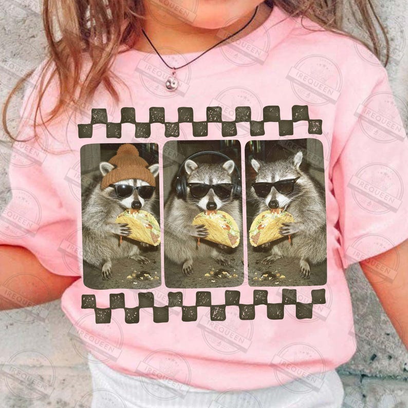 May include: A pink t-shirt with a graphic of three raccoons wearing sunglasses and eating tacos. The raccoons are in a framed design with a black and white checkered border. The shirt has the text "IREQUEEN" printed on it.