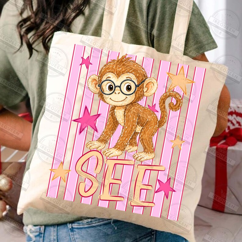 Puede incluir: Un bolso tote beige con un mono de dibujos animados con gafas, sobre un fondo de rayas rosas con estrellas. La palabra "SEE" se muestra en una fuente l&uacute;dica debajo del mono. El bolso lo sostiene una persona.