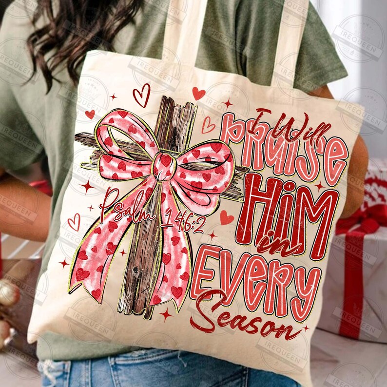 May include: A beige tote bag featuring a wooden cross with a pink bow adorned with red hearts. The bag has the text "I Will Praise Him in Every Season" and "Psalm 146:2" in red. Small red hearts and stars are scattered around the design.