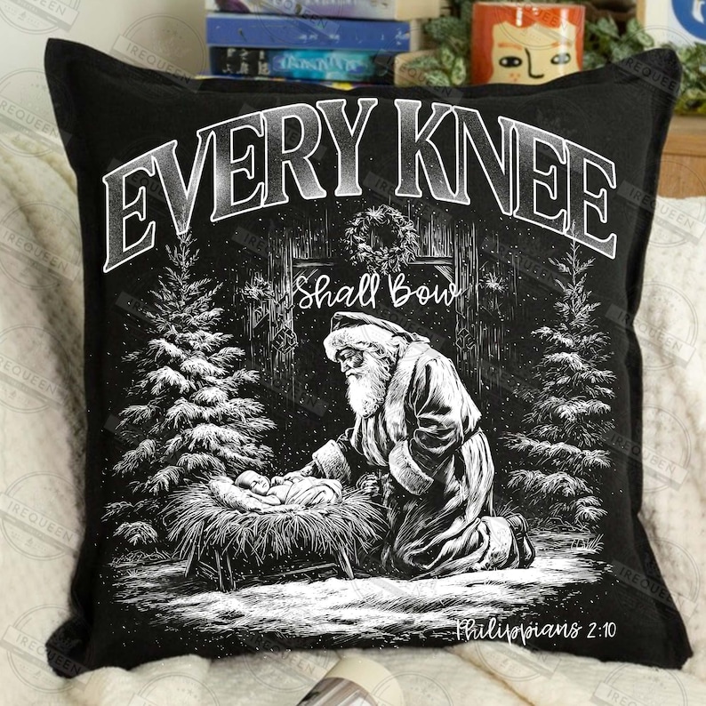 May include: Black decorative pillow with a Christmas scene. The pillow features a black and white illustration of Santa Claus kneeling before baby Jesus. The text "EVERY KNEE SHALL BOW" is at the top, with "Philippians 2:10" at the bottom.