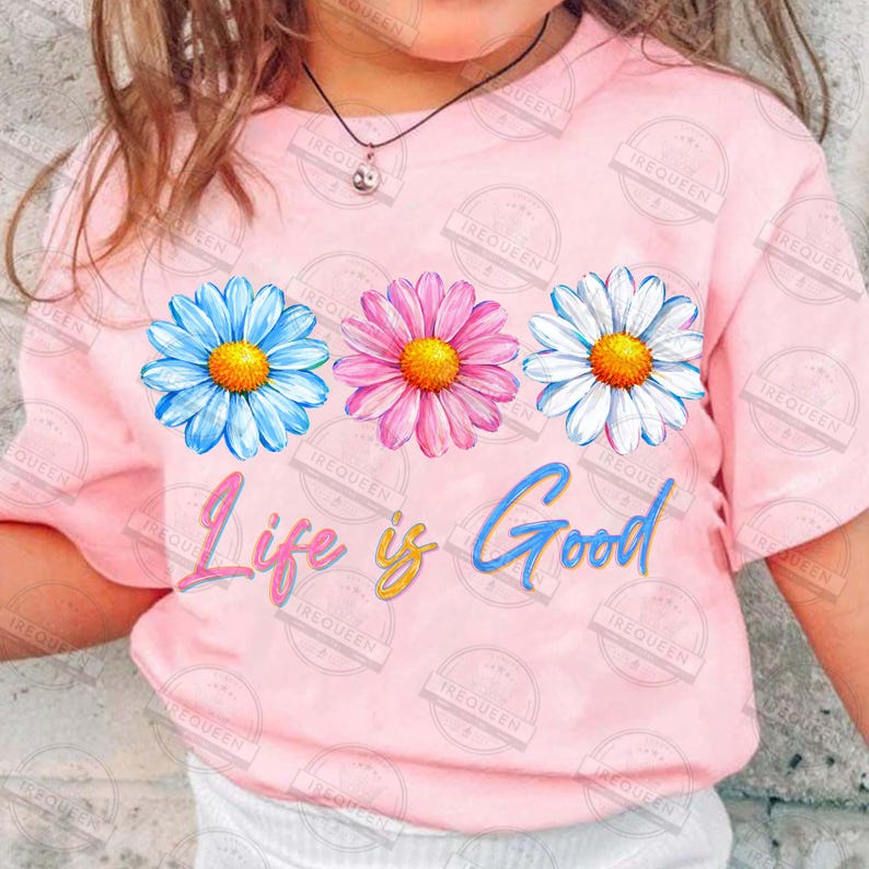 Pu&ograve; includere: T-shirt rosa chiaro con tre fiori di margherita colorati in blu, rosa e bianco con centri gialli. La frase "Life is Good" &egrave; scritta sotto in un carattere corsivo colorato. Una maglietta casual.