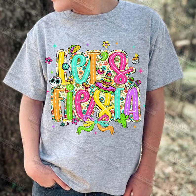 May include: A grey t-shirt featuring the phrase "Let's Fiesta" in vibrant, decorative lettering. The design incorporates a sombrero, cactus, taco, and floral patterns, ideal for a celebration.
