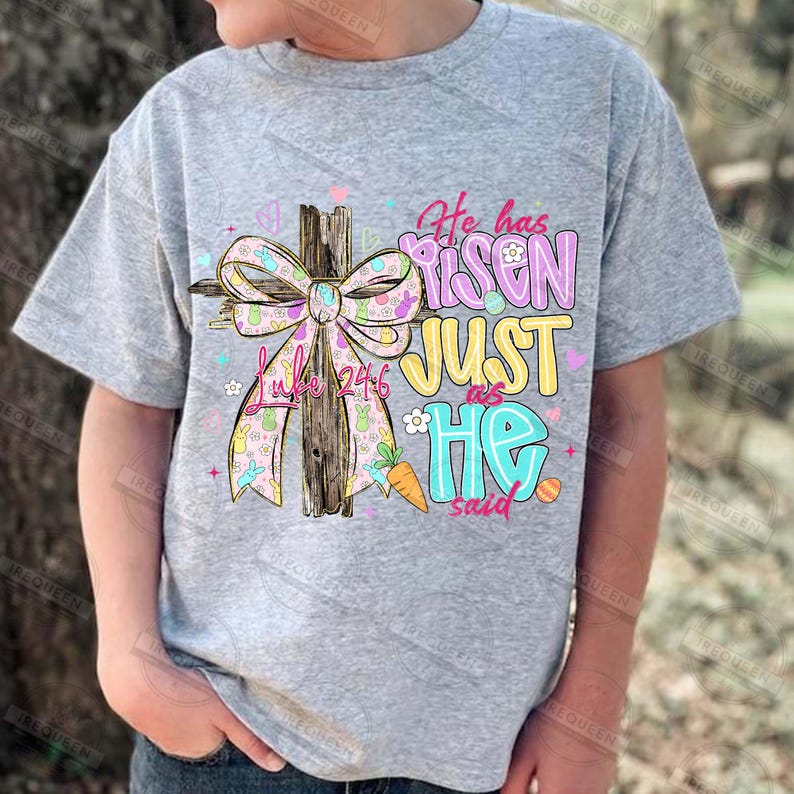 May include: A gray t-shirt featuring a colorful graphic design. The design includes a wooden cross with a decorative bow, text that reads "He has Risen Just as He said," and the Bible verse Luke 24:6. Easter themed.