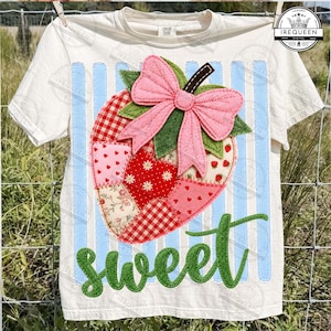 Puede incluir: Camiseta color crema con un diseño de fresa de patchwork, un lazo rosa y hojas verdes. La fresa está hecha de varias telas estampadas. Rayas verticales azul claro y la palabra "sweet" en escritura verde también están en la camiseta.