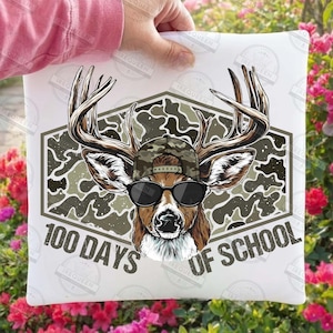Puede incluir: Coj&iacute;n blanco con un gr&aacute;fico de un ciervo con gafas de sol y gorra de camuflaje. El ciervo est&aacute; dentro de un hex&aacute;gono de camuflaje con el texto "100 DAYS OF SCHOOL" en fuente curva.