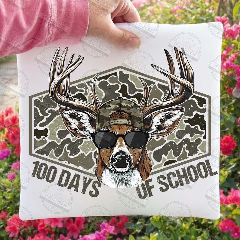 Puede incluir: Coj&iacute;n blanco con un gr&aacute;fico de un ciervo con gafas de sol y gorra de camuflaje. El ciervo est&aacute; dentro de un hex&aacute;gono de camuflaje con el texto "100 DAYS OF SCHOOL" en fuente curva.