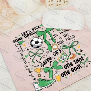 May include: A pink and green mousepad with a soccer theme. It features a soccer ball, a trophy, a hot dog, a drink, and a shoe. The text on the mousepad reads "Let's kick some grass", "Game Day", "My heart is on that field", "One shot one goal".