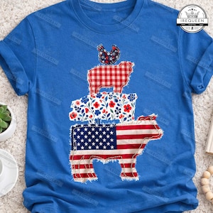 May include: Blue t-shirt featuring a stacked design of a cow, pig, sheep, and chicken. The cow is designed with the American flag, the sheep in red gingham, and the pig with a floral pattern. The chicken has a floral pattern.