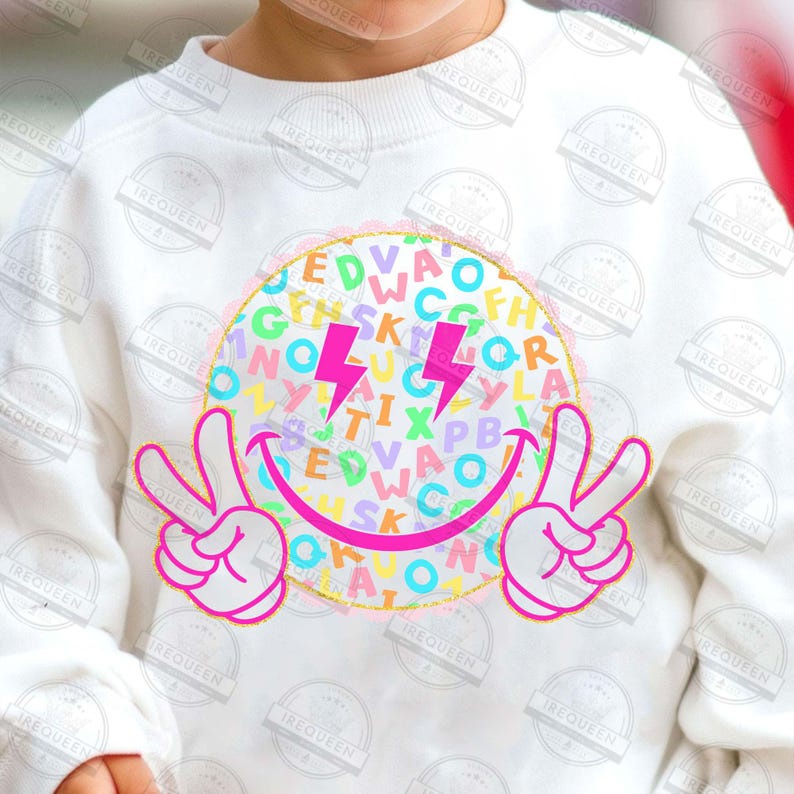 May include: White sweatshirt featuring a large, colorful smiley face design. The design includes a circle filled with letters, two pink lightning bolts, and peace signs. The smiley face has a pink outline.