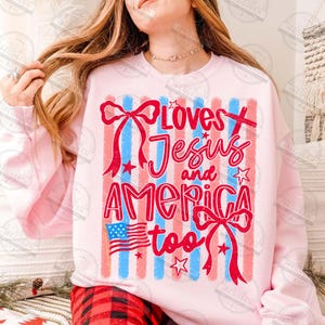 Puede incluir: Sudadera rosa claro con el texto "Loves Jesus and America too" en rojo y azul. El dise&ntilde;o incluye una bandera estadounidense, lazos y estrellas, con rayas verticales rojas y azules en el fondo.