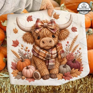 May include: A white fabric square featuring a printed illustration of a fluffy brown Highland cow wearing a plaid bow and scarf, surrounded by autumn leaves, wheat stalks, and pumpkins in shades of orange, brown, and muted pink.