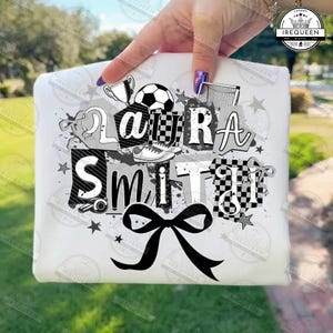 Könnte beinhalten: Weißes T-Shirt mit einem schwarz-grauen Design mit dem Namen "Laura Smith". Das Design enthält fußballbezogene Elemente wie einen Fußball, eine Trophäe und einen Fußballschuh sowie eine große schwarze Schleife.