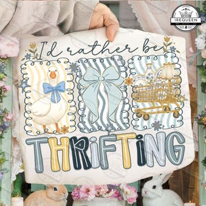Puede incluir: Un letrero decorativo con el texto "I'd rather be thrifting". El letrero presenta ilustraciones de un ganso con un lazo azul, un lazo azul y un carrito de compras lleno de artículos. La paleta de colores incluye azul, amarillo y blanco.