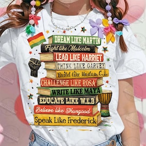 May include: White t-shirt featuring a stack of books with inspirational phrases like "Dream Like Martin" and "Fight Like Malcolm." The design includes a black power fist, a small flag, and a drum. The shirt is adorned with star accents.